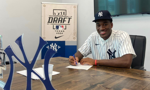  Dillon Lewis sits at a table signing New York Yankees drafting papers